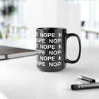 A 15 oz black ceramic mug with a repeating white 'NOPE' text pattern, sitting on a white desk with a blurred notebook and pen in the background.