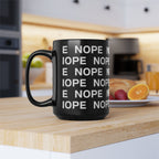 A 15oz black ceramic mug with white text repeating 'NOPE' sits on a wooden countertop in a blurred kitchen setting with breakfast items in the background.